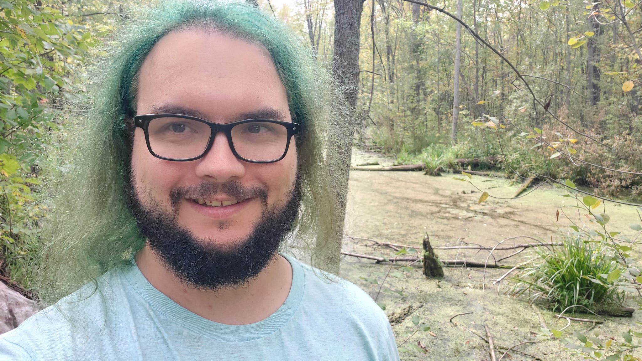 A man with green hair stands in front of a wetland, Photo 1